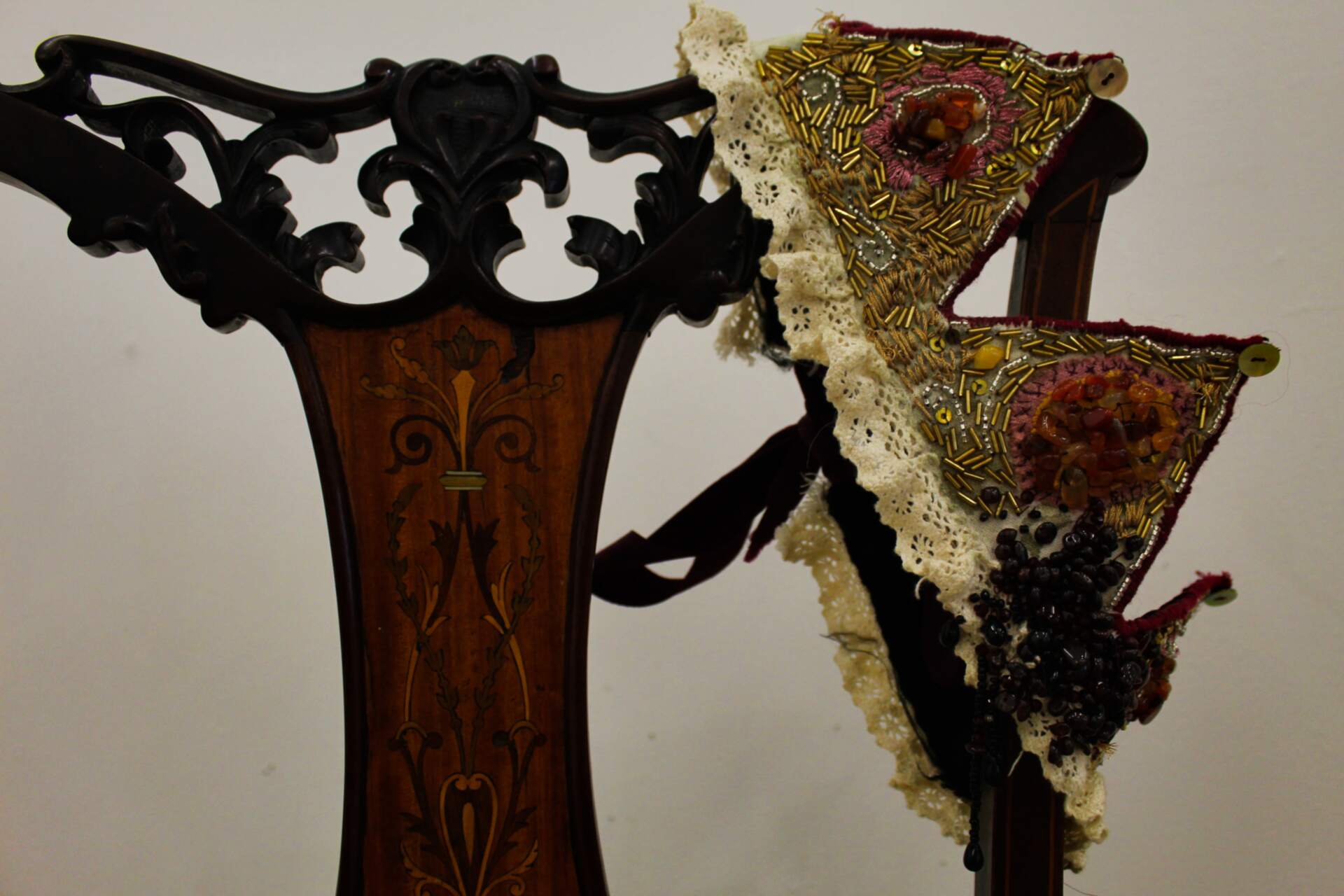 A fabric crown with gold beading, and orange, pink, and red stones and thread, hangs off a chair.