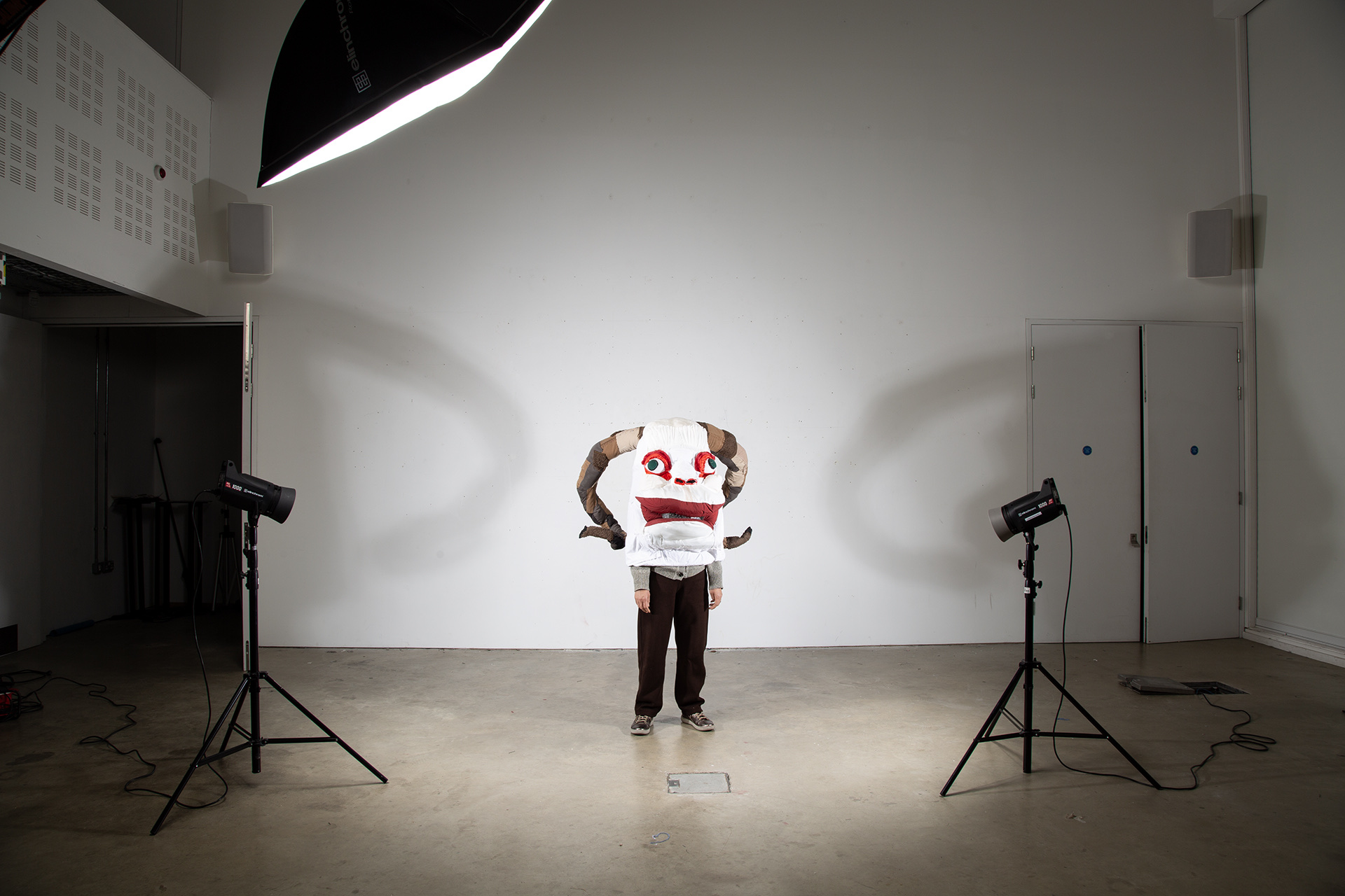 Large fabric creature costume with big eyes, red mouth, and spiralled horns worn over the head.